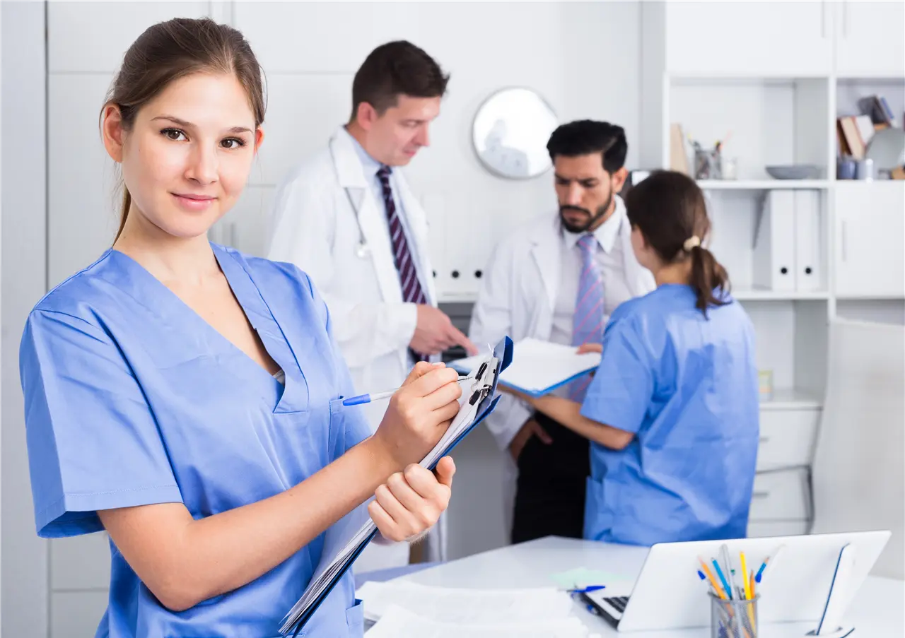 In einem Krankenhaus bespricht das medizinische Team in blauer und weißer Arbeitskleidung Unterlagen, während eine Person im Vordergrund Notizen macht.